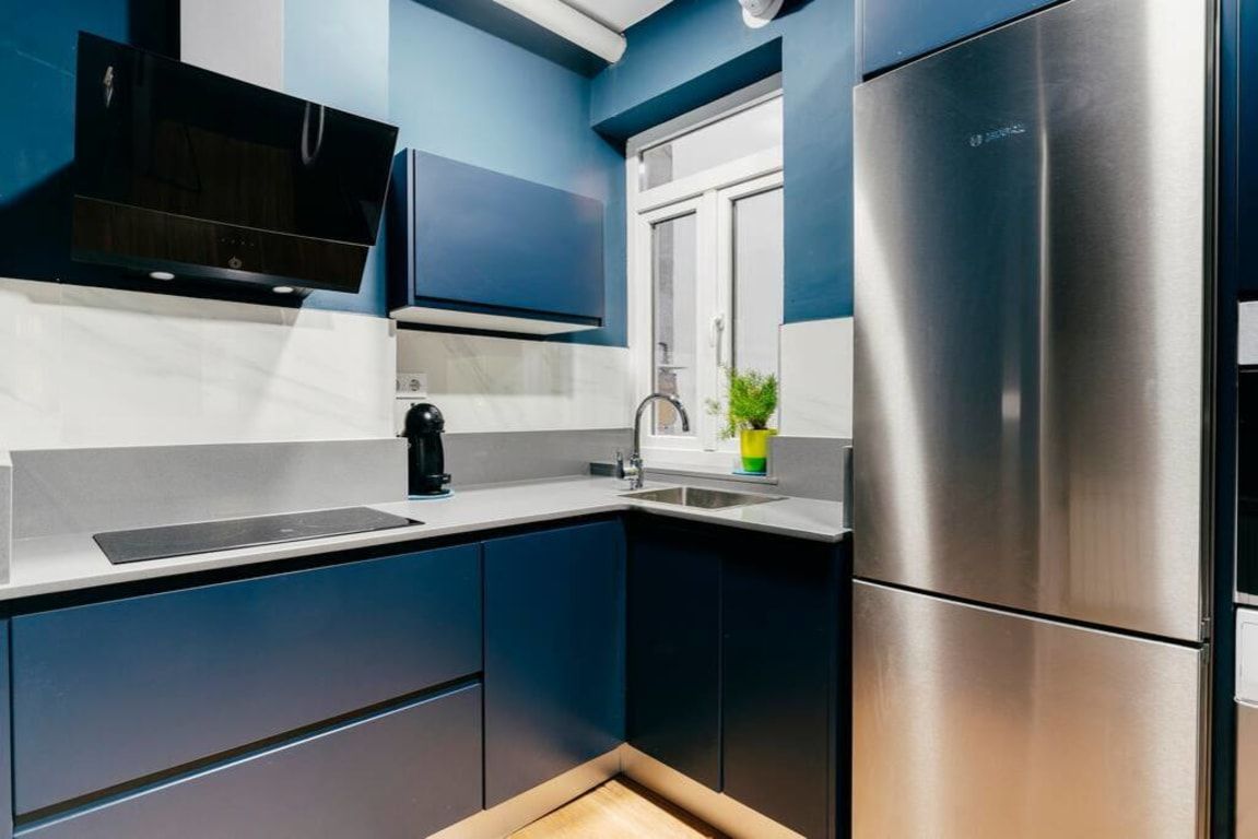 A modern kitchen with dark blue cabinets, a stainless steel refrigerator, and a built-in oven.