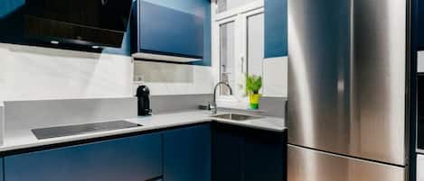 A modern kitchen with dark blue cabinets, a stainless steel refrigerator, and a built-in oven.