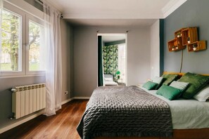 Een slaapkamer met een bed, een radiator, een raam met gordijnen en uitzicht op een balkon.