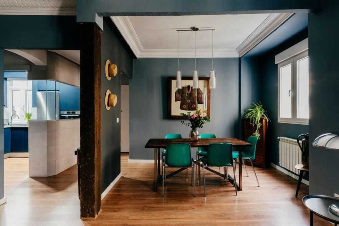 Un comedor con una mesa de madera y sillas verdes, un ventilador de techo y una ventana que da a la cocina.