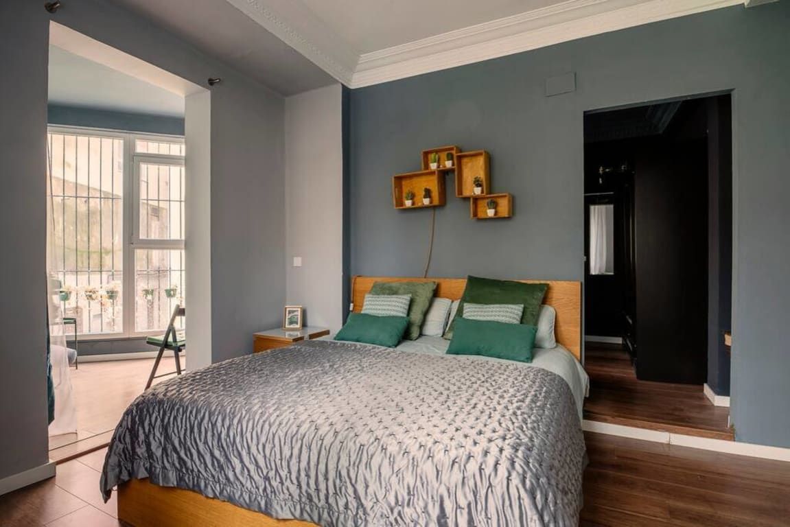 Une chambre à coucher comprenant un lit, une table de chevet, une fenêtre et une porte donnant sur une autre pièce.