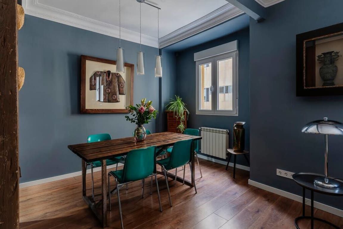 Un comedor con una mesa de madera y sillas color turquesa, una planta en maceta e iluminación colgante.