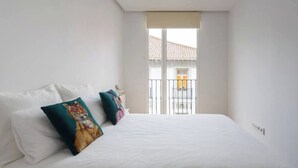A bedroom with a large bed, two pillows, a window with a view of buildings, and a balcony. - Piso moderno en el centro (Santander)