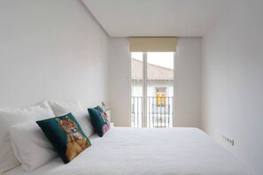 Ein Schlafzimmer mit einem großen Bett, zwei Kissen, einem Fenster mit Blick auf Gebäude und einem Balkon.