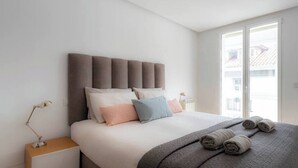 A modern bedroom with a large bed, a headboard, bedside lamps, and a view through a window. - Piso moderno en el centro (Santander)