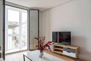 A modern living room with a television, a glass coffee table, and a sliding glass door leading to a balcony. - Piso moderno en el centro (Santander)