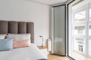A bedroom with a bed, pillows, a bedside lamp, and a sliding glass door leading to a balcony. - Piso moderno en el centro (Santander)