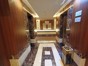 Un hall d’hôtel moderne avec un sol en marbre, des panneaux de bois et un comptoir d’accueil.