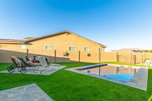 Et hus med swimmingpool, grøn græsplæne og en terrasse med liggestole.