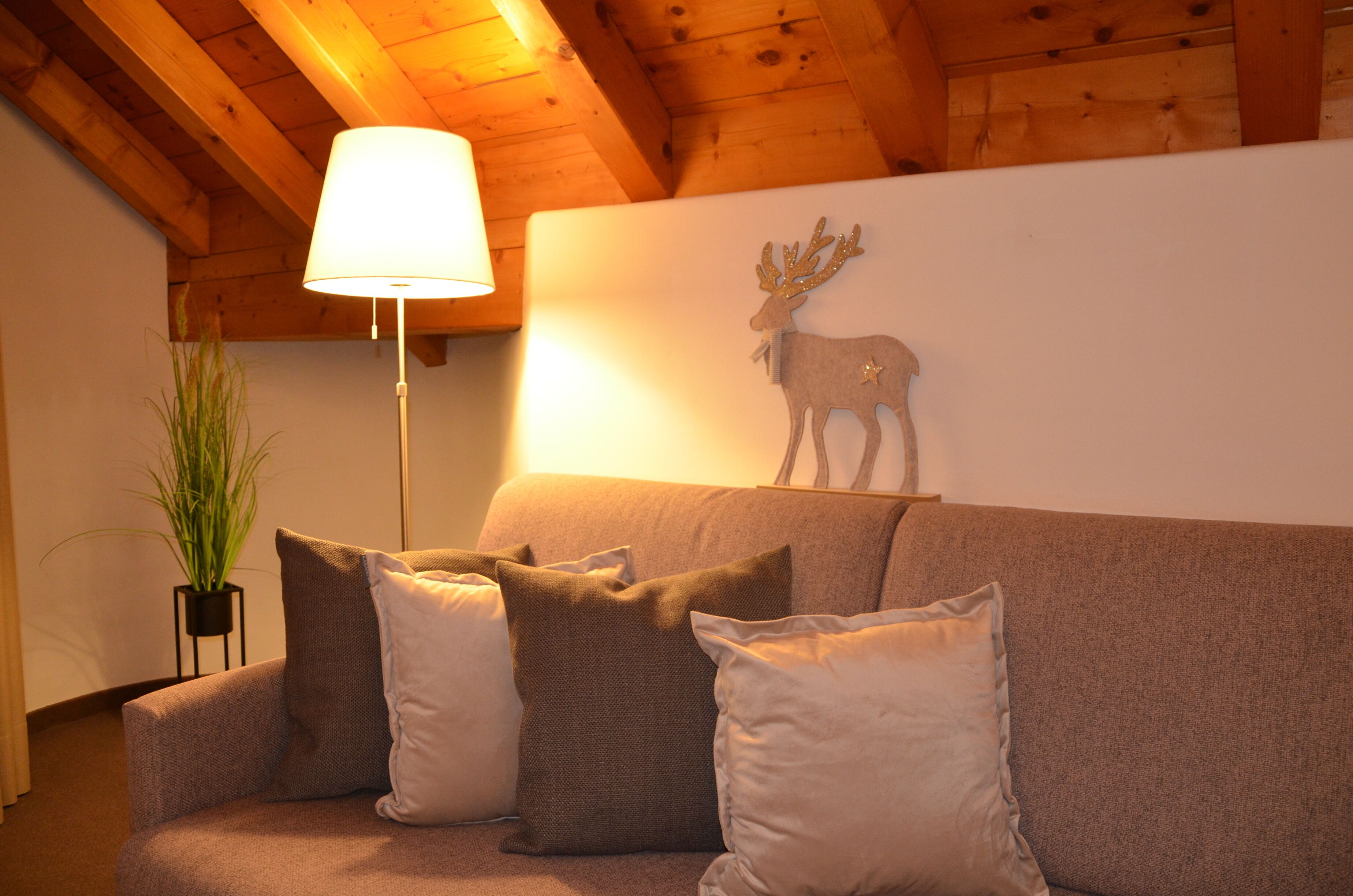 Een gezellige woonkamer met een bank, kussens, een lamp en een herten decoratie aan de muur.