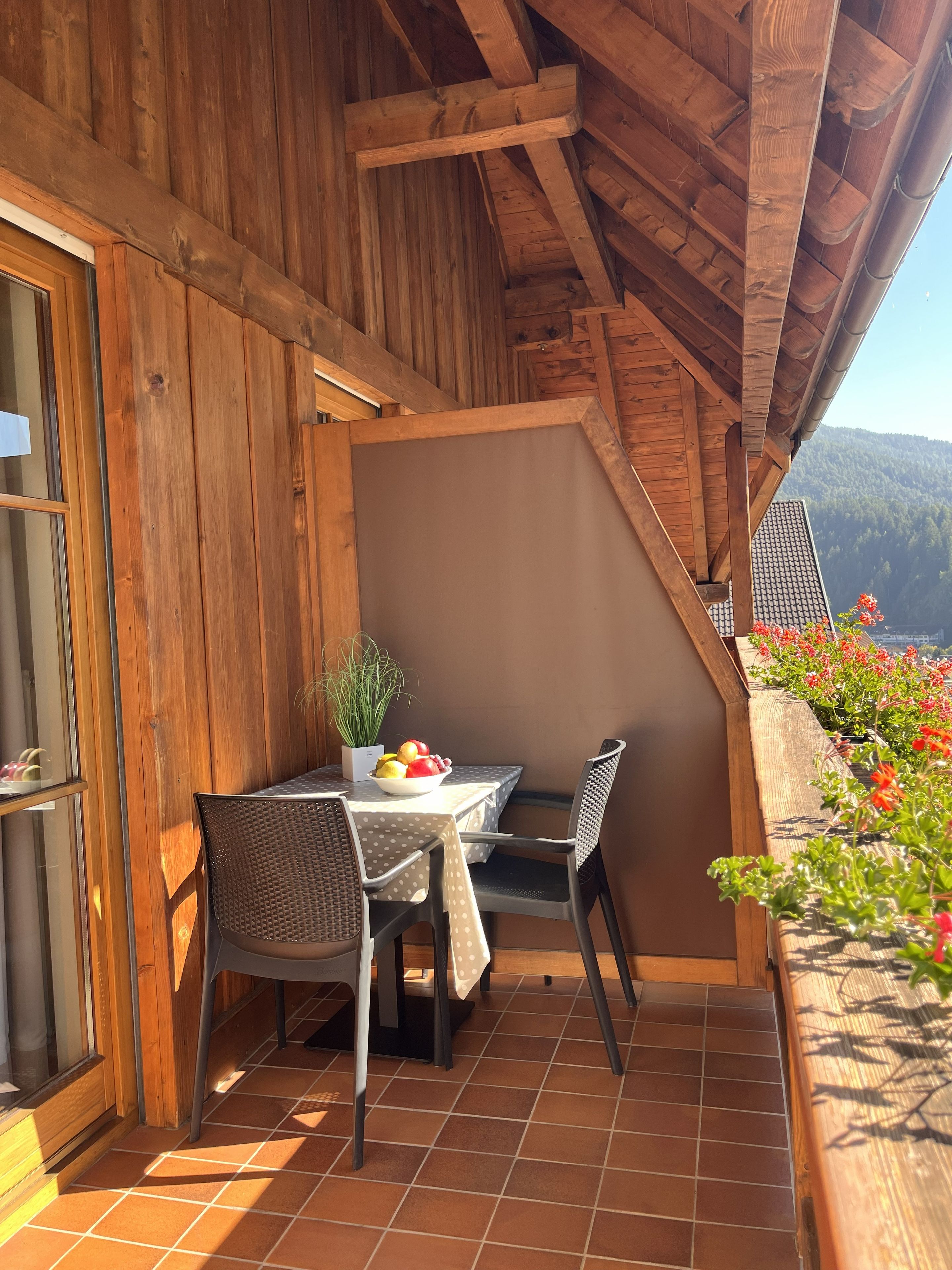 Varanda de madeira com mesa, cadeiras, um vaso de planta e vista para a montanha.