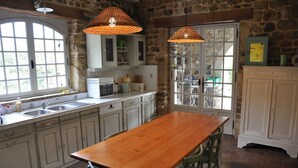 A kitchen with a wooden table, green chairs, white cabinets, and two hanging lamps.