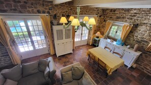 A cozy room with a stone wall, a dining table with chairs, a sofa, and a chandelier.