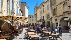An outdoor café with tables and chairs, surrounded by historic buildings with stone facades and traditional shutters.