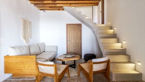 Ein gemütlicher Wohnbereich mit Holzboden, einer Couch, zwei Korbstühlen, einem kleinen runden Tisch und einer Treppe mit beleuchteten Stufen.