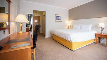 Een hotelkamer met een bed, een bureau, een stoel, een lamp en een schilderij aan de muur.
