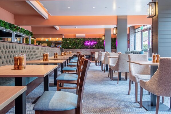 Un restaurante con una barra alargada, asientos acolchados y un letrero de neón.