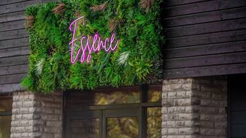 A building facade with a neon sign spelling 'Essence' amidst lush greenery.