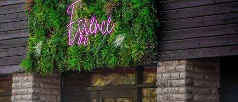 A building facade with a neon sign spelling 'Essence' amidst lush greenery.