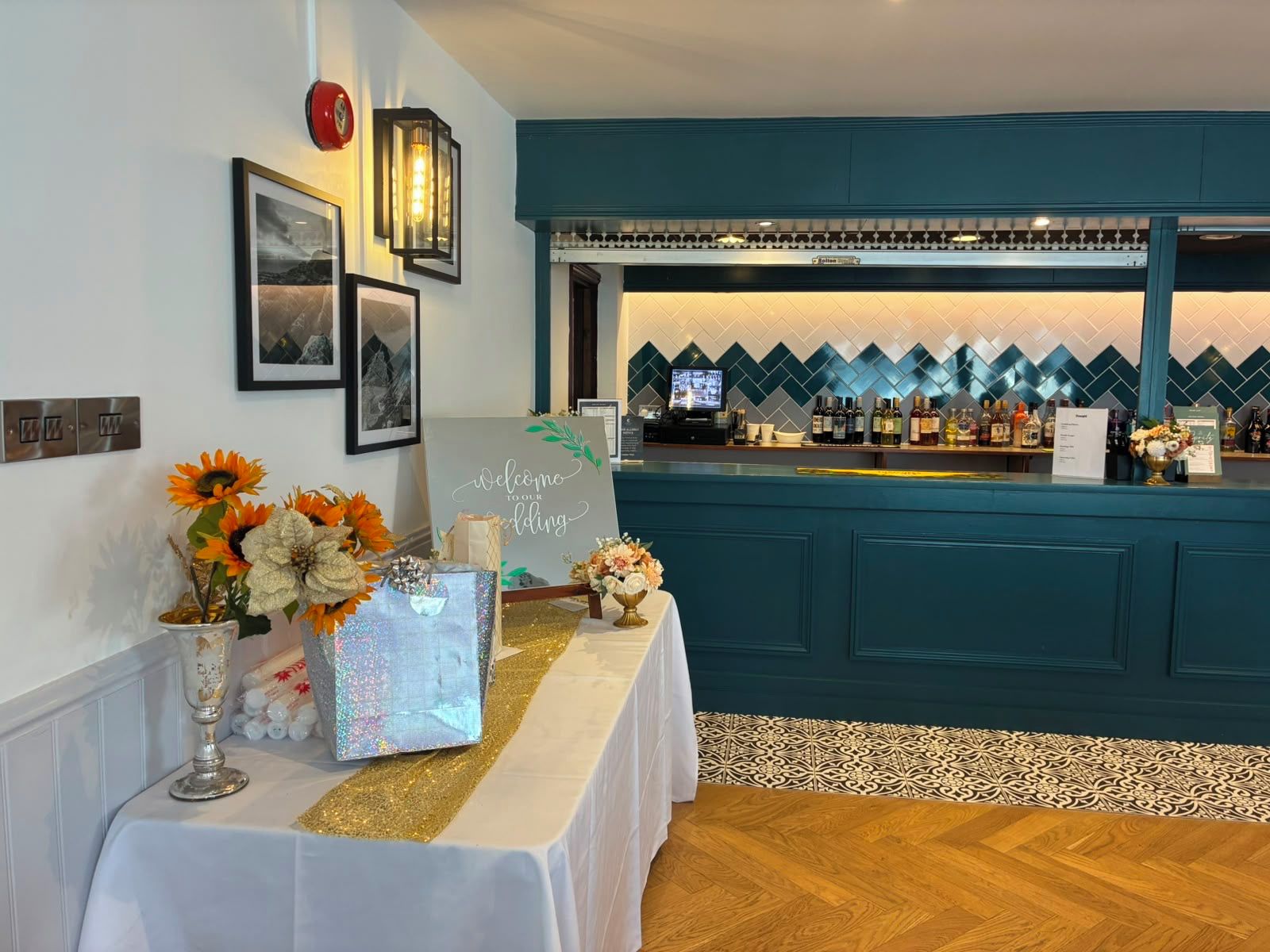 A bar area with a teal-colored counter, a television, and a decorative wall with a diamond pattern.