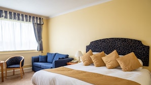Een hotelkamer met een groot bed, een blauwe bank, een stoel en een nachtkastje met een lamp.