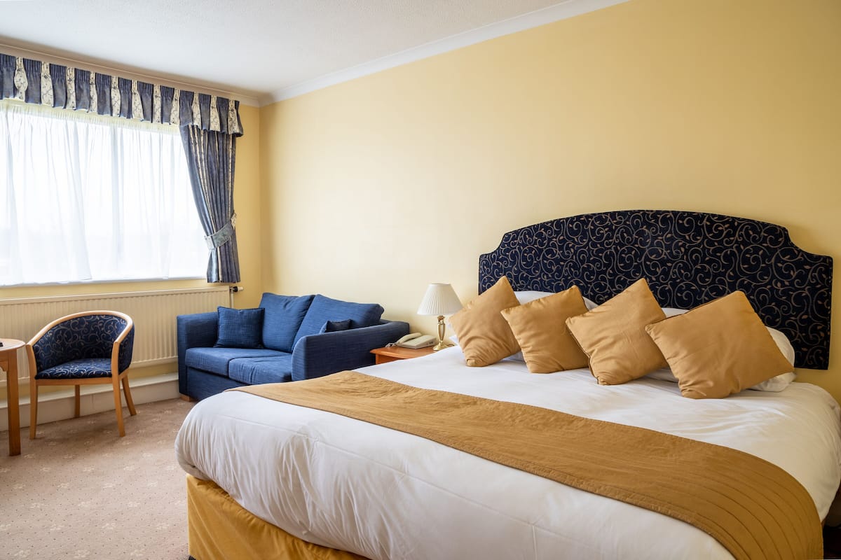 Ein Hotelzimmer mit einem großen Bett, einem blauen Sofa, einem Sessel und einem Nachttisch mit Lampe.