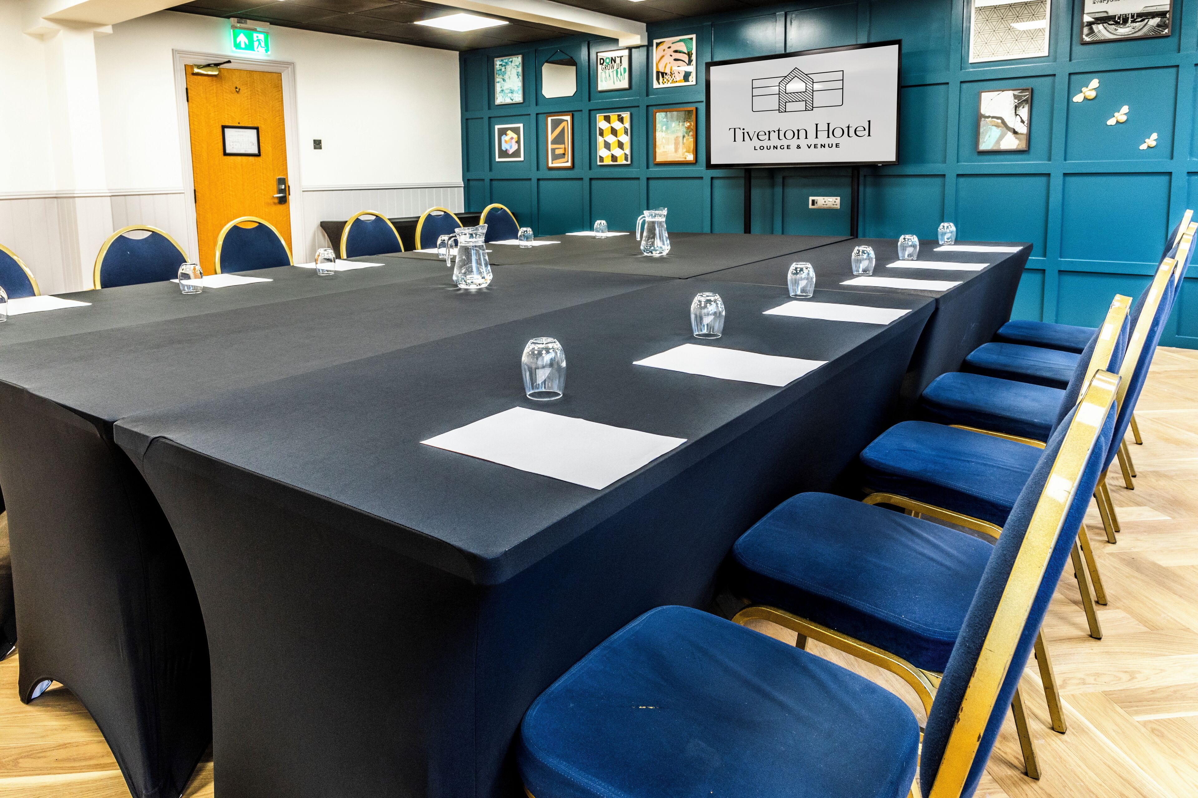 A conference room with a long table, blue chairs, and a projector screen displaying the hotel name.