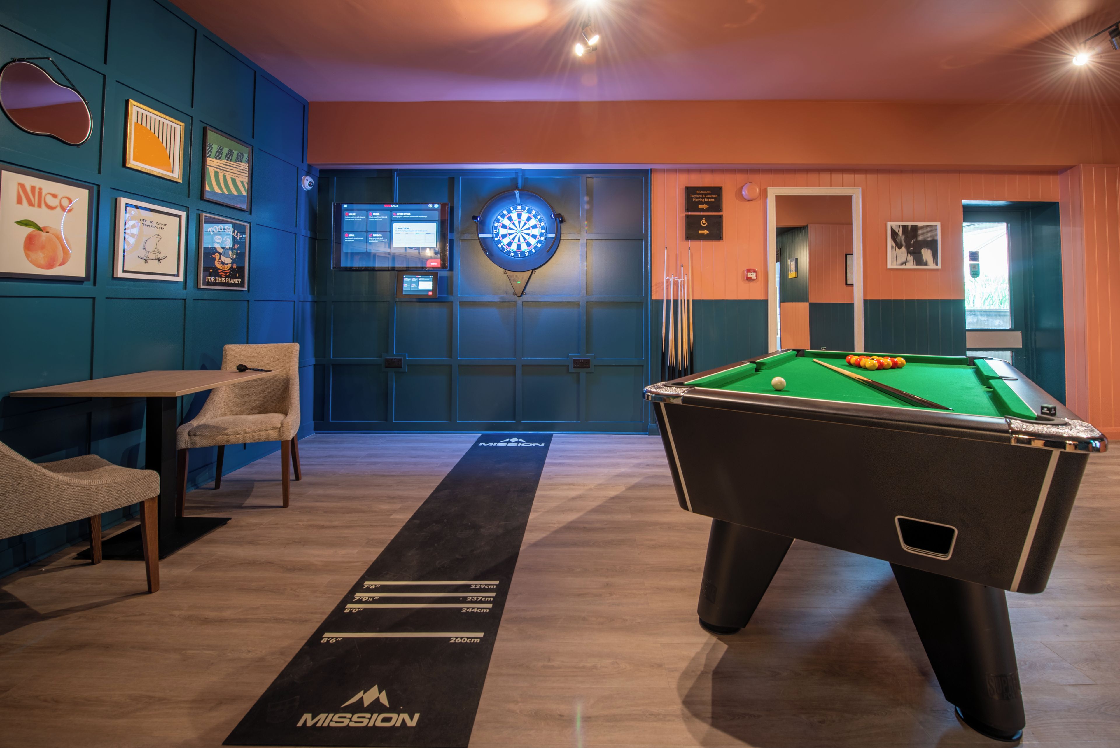 Ein Billardtisch mit Dartscheibe, ein weiterer Billardtisch und eine Lounge-Ecke mit Sesseln und Tisch.