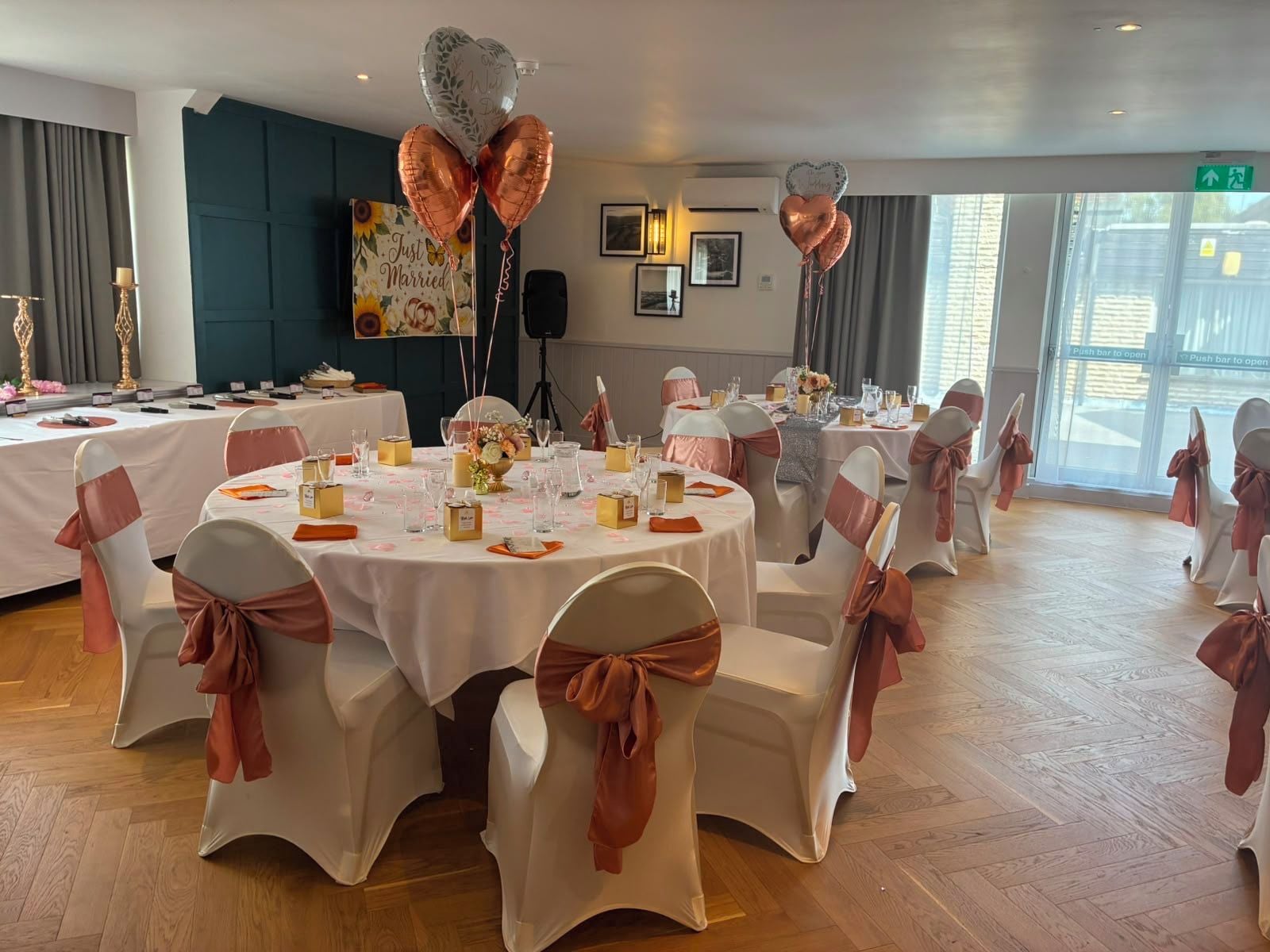 A banquet hall with round tables, white chairs with brown sashes, and heart-shaped balloons.