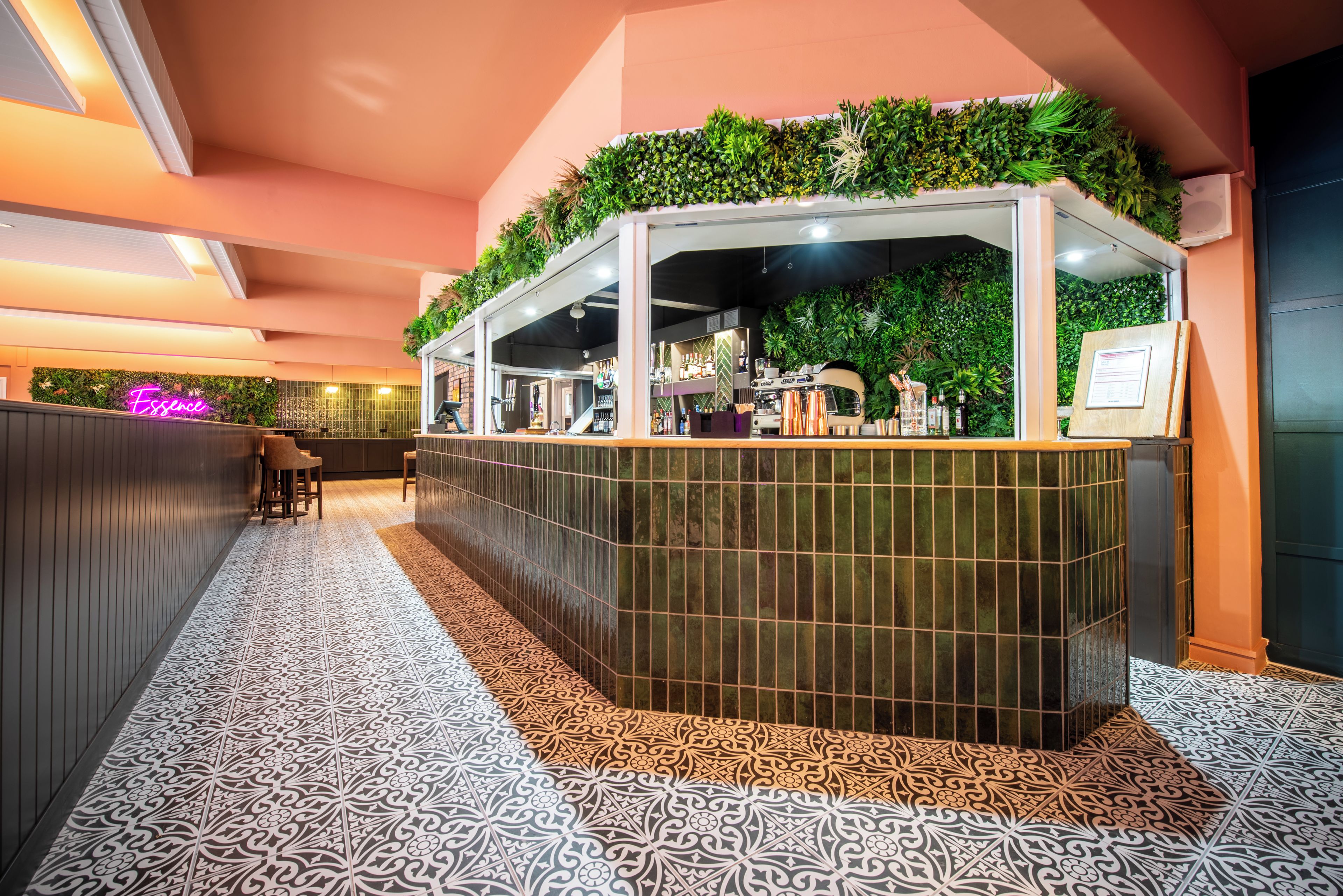A bar area with a green plant wall, a patterned floor, and a neon sign.