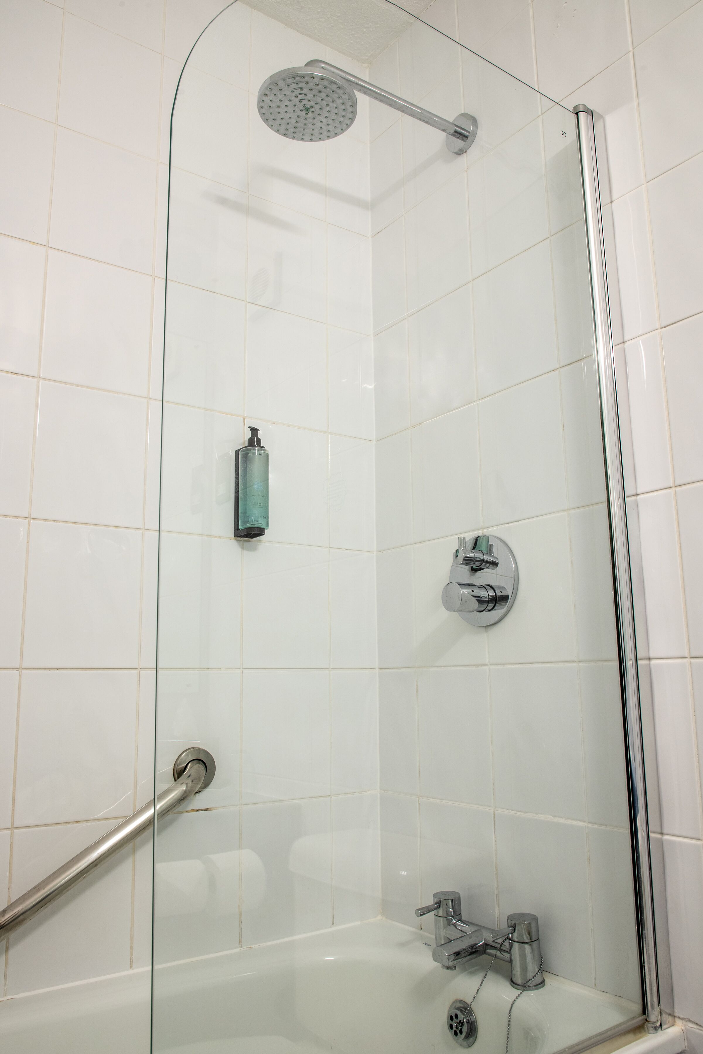 Eine moderne Dusche mit Glastrennwand, Duschkopf, Seifenspender und Armatur.
