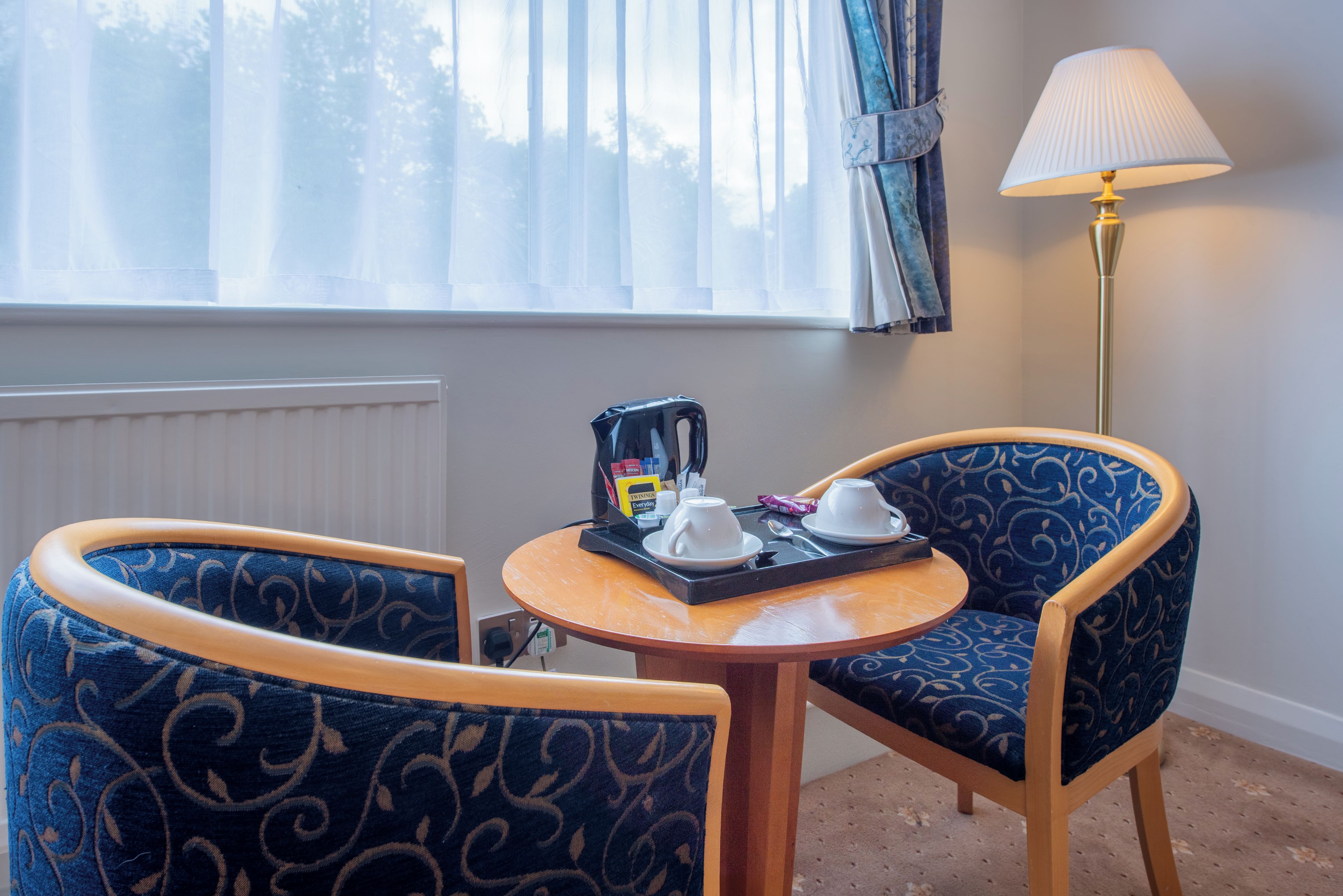 A room with a small table and two chairs, a lamp, and a window with curtains.