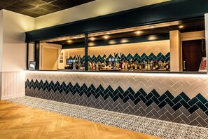 Eine Bar mit einer Wand aus gemusterten Fliesen, Holzboden und einer Auswahl an Flaschen hinter der Theke.