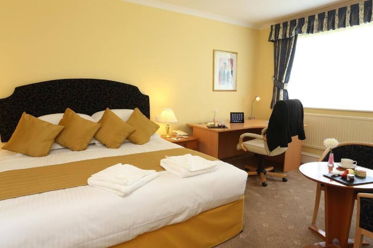 Ein Hotelzimmer mit Bett, Schreibtisch, Stuhl und einem kleinen Tisch mit Tasse und Untertasse.