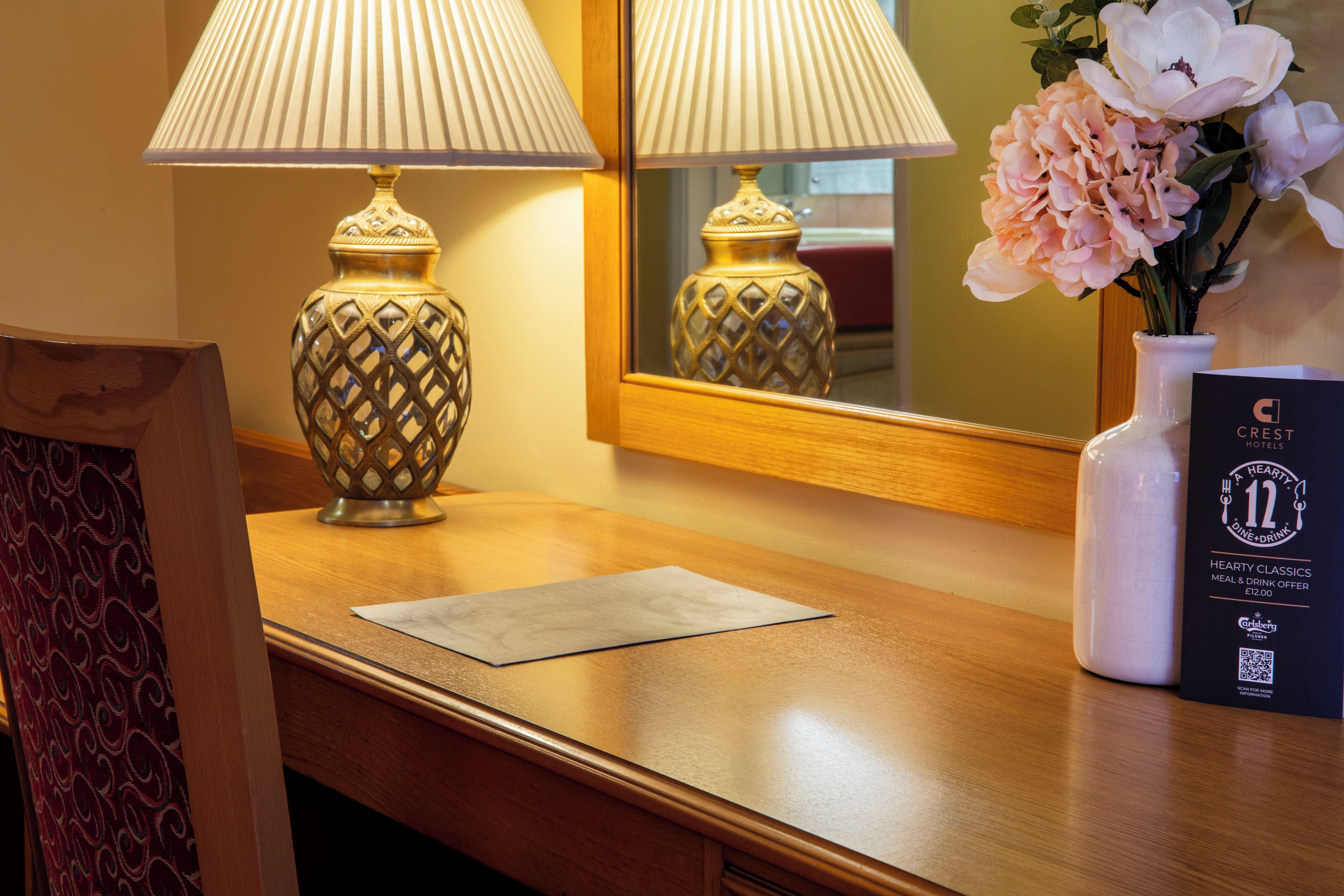 En hotelfacade med to lamper, en vase med blomster og et reklamekort.