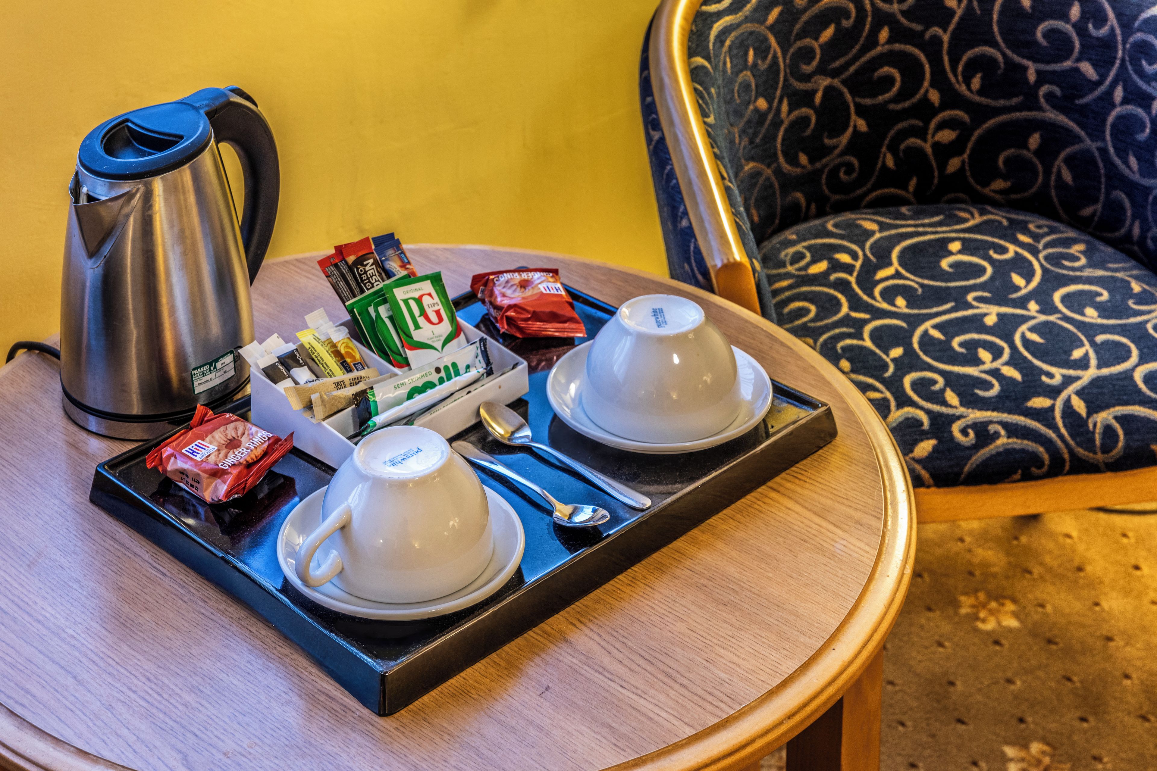 A tray with two white cups, a kettle, and various food items on a small round table.