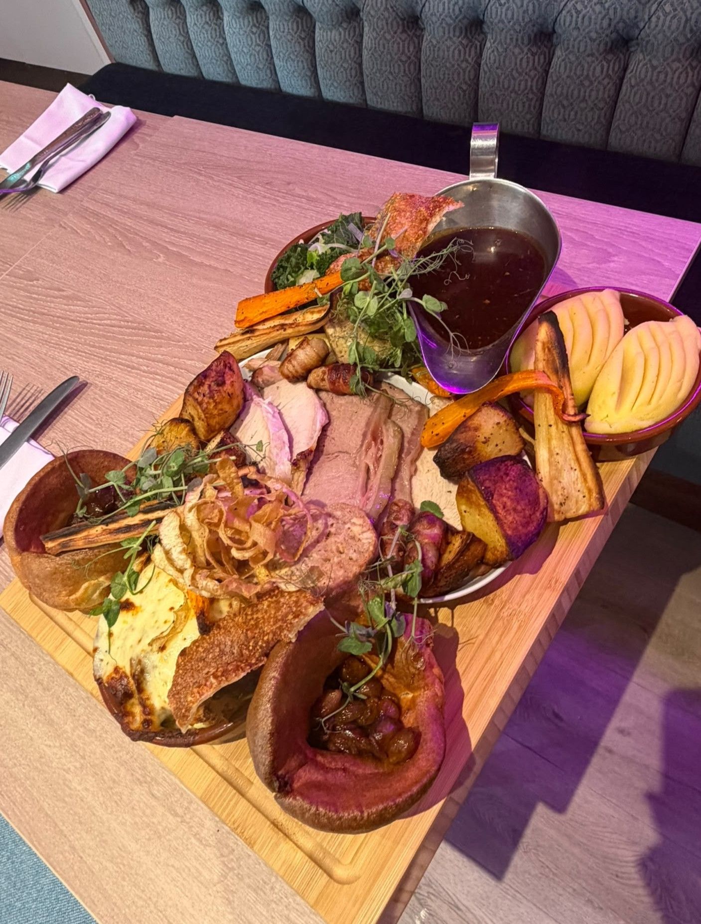 Ein Holzservierbrett mit verschiedenen gebratenen Fleischsorten, Gemüse und einer Soße.