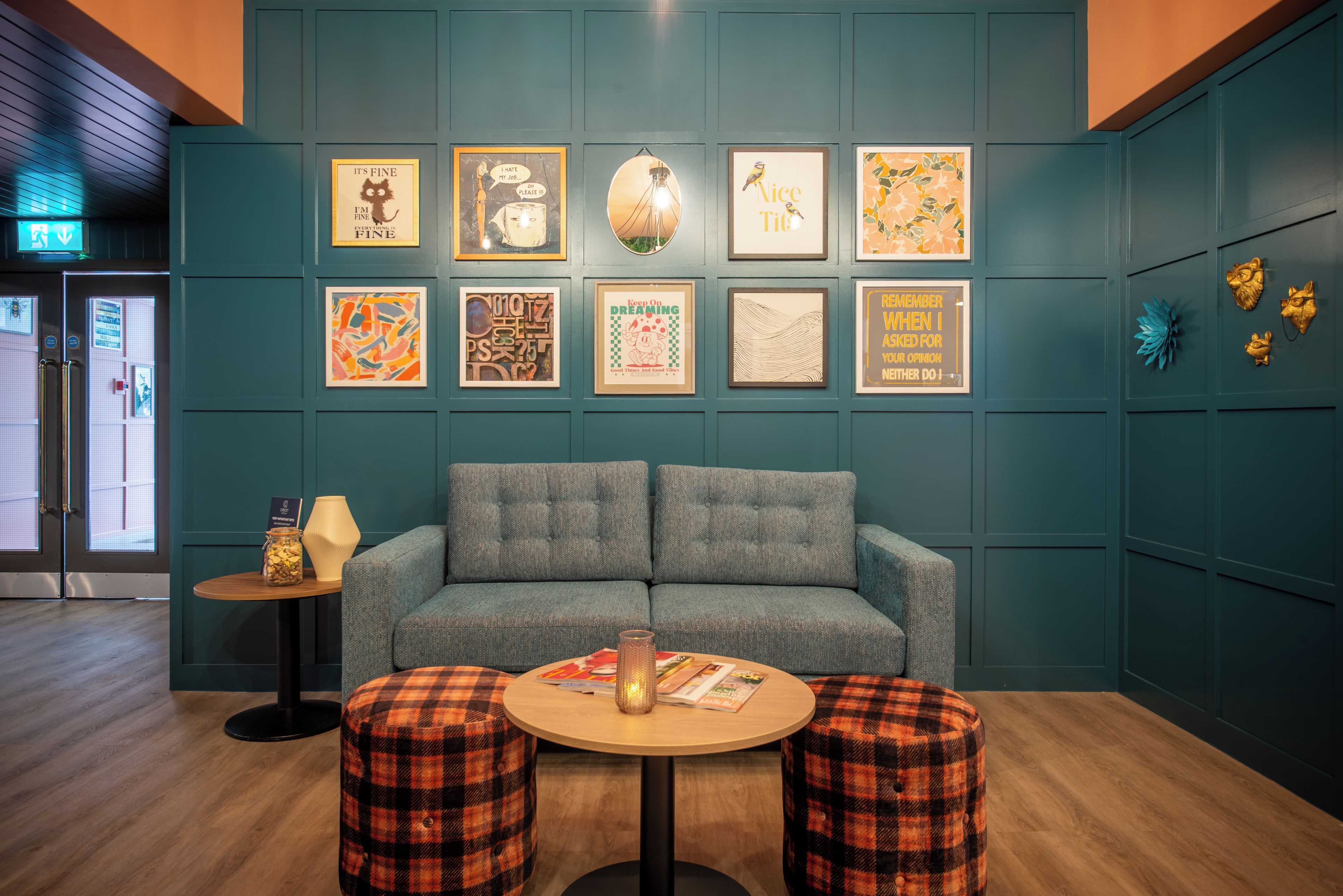 A room with teal walls, a grey sofa, two plaid ottomans, and various framed artworks.