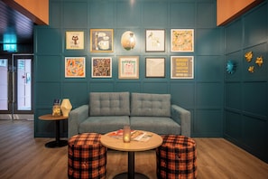 Una habitación con paredes color turquesa, un sofá gris, dos otomanas a cuadros y varias obras de arte enmarcadas.