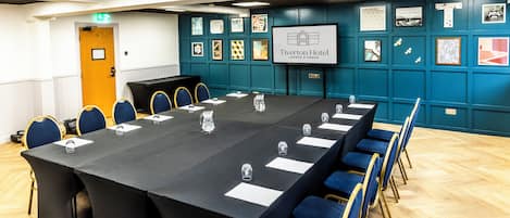 A conference room with a long table, blue chairs, and a screen displaying the hotel name.