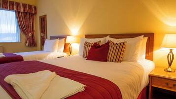 A hotel room with two beds, each with a wooden headboard, white bedding, and red accents. There are bedside lamps and a wooden nightstand with a drawer.