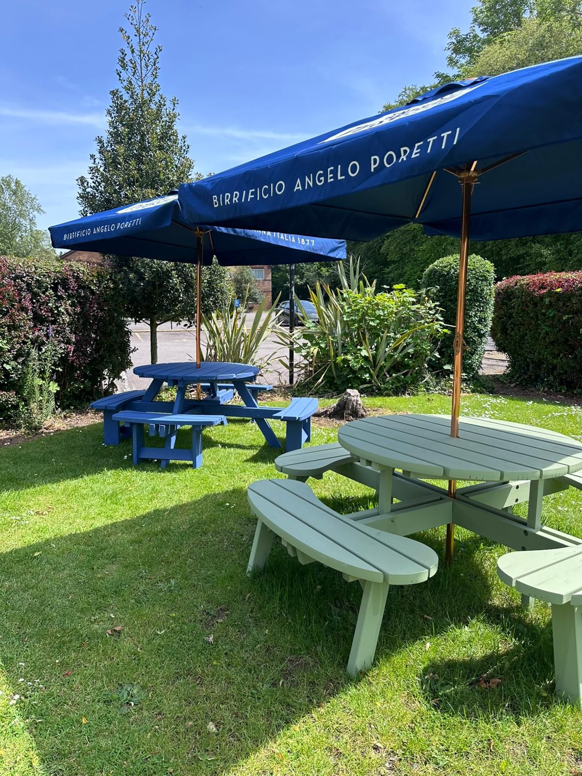 An outdoor seating area with picnic tables and blue umbrellas labeled 'Birrificio Angelo Poretti.'