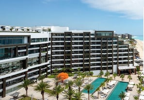 Un hotel moderno con varios pisos, una zona de piscina con tumbonas y vistas a la playa.