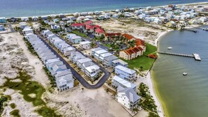 Vue aérienne d’une zone résidentielle côtière comprenant plusieurs bâtiments, une plage et une jetée.