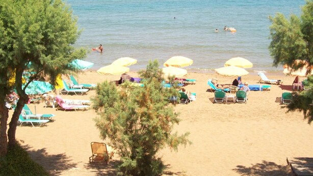 A beach with several sun loungers and umbrellas, a clear view of the sea, and a few people swimming. - Kato Stalos Beach (Chania)