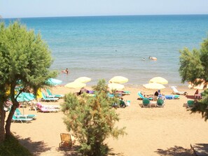 A beach with several sun loungers and umbrellas, a clear view of the sea, and a few people swimming. - Kato Stalos Beach (Chania)