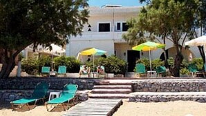 A pool area with lounge chairs and umbrellas, surrounded by trees and a building in the background. - Kato Stalos Beach (Chania)