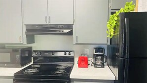 Una cucina con un piano cottura nero, un tostapane rosso, una macchina da caffè e un frigorifero.
