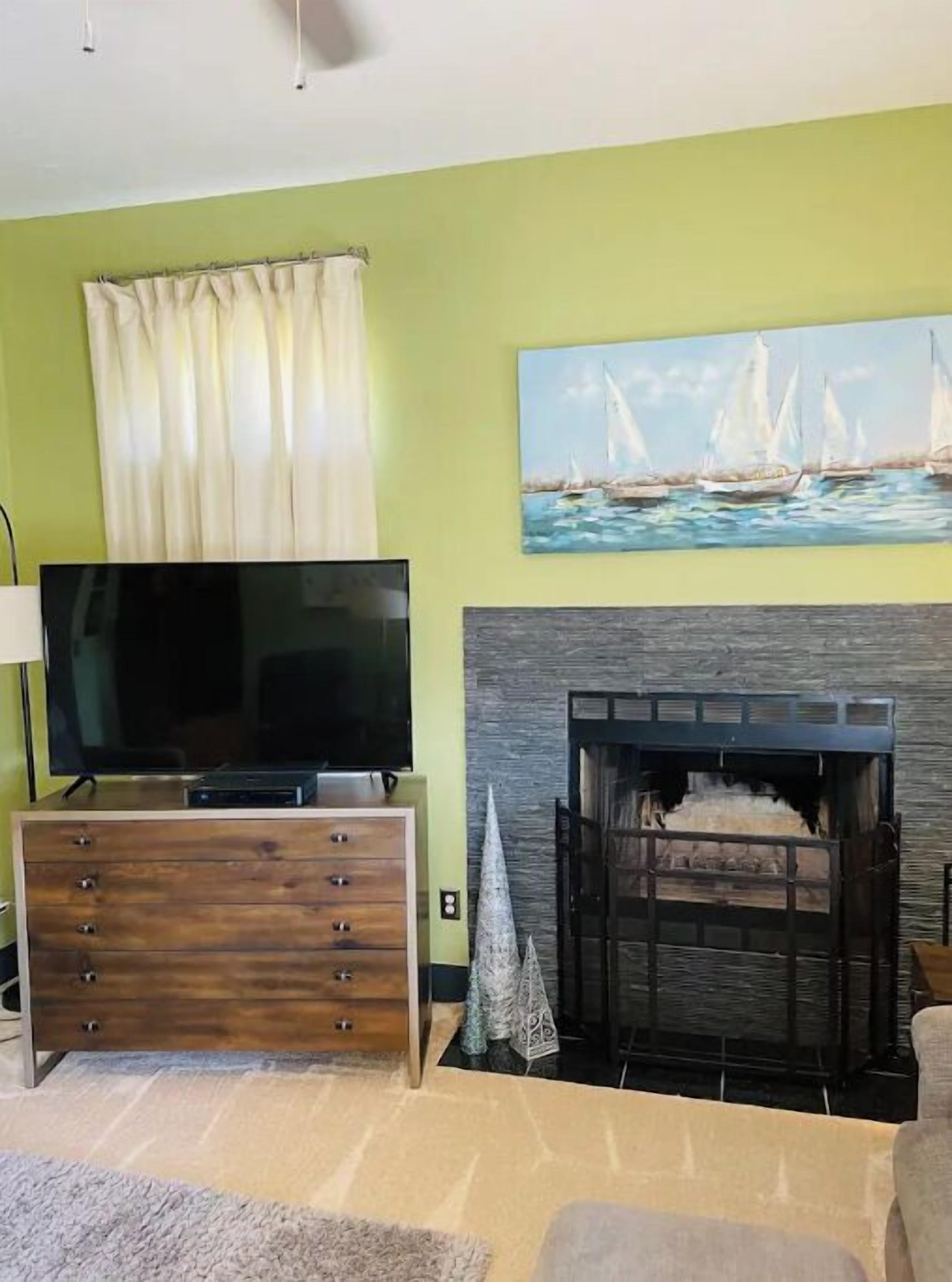 Una sala de estar con televisor, chimenea y un cuadro de veleros.