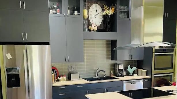A modern kitchen with dark cabinets, stainless steel appliances, a central island, and a red chair. - Remodeled 3 Bedroom Home, Fireplace & Large Yard (Yukon)